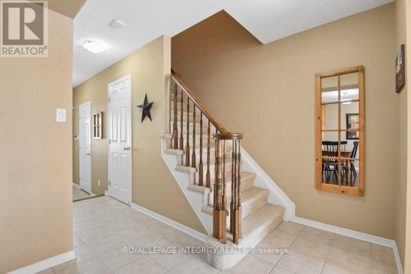 Staircase with beige carpeted steps and a wooden banister leading up from the tiled hallway. - 416 Wisteria Crescent, Ottawa