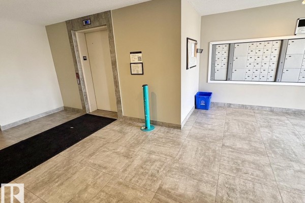 Building lobby with elevator, mailboxes, blue recycling bin, and a teal post. - #417 5404 7 Av Sw, Edmonton