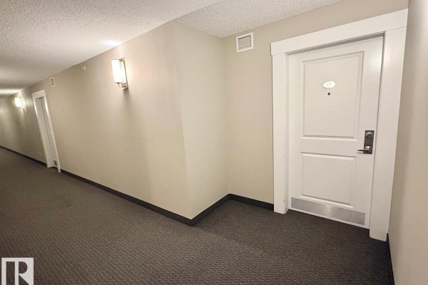Apartment building hallway with carpet, wall sconces, and a white door on the right. - #417 5404 7 Av Sw, Edmonton
