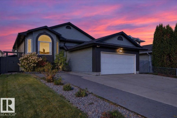 Exterior of a grey house at dusk with a colorful sunset sky and illuminated windows. - 417 Hollick Kenyon Rd Nw Nw, Edmonton
