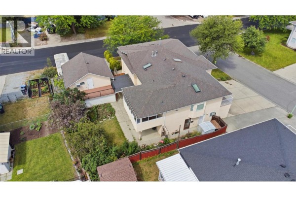 Aerial view of the rear of the beige stucco house with a covered deck and surrounding trees and fencing. - 417 Wigglesworth Crescent, Kelowna