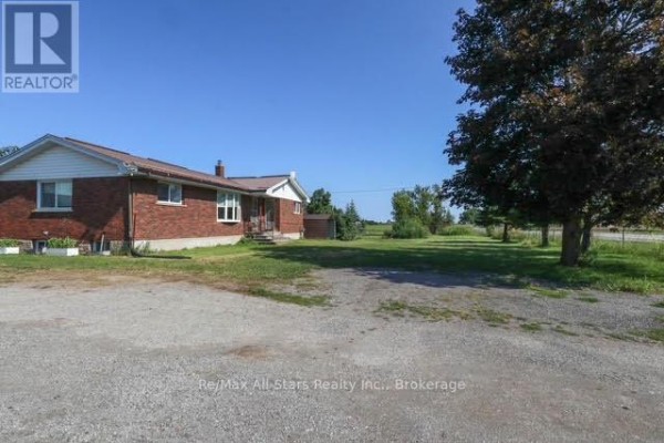 Side view of a red brick house with a gravel driveway and surrounding green trees. - 4175 Highway 35 N, Kawartha Lakes
