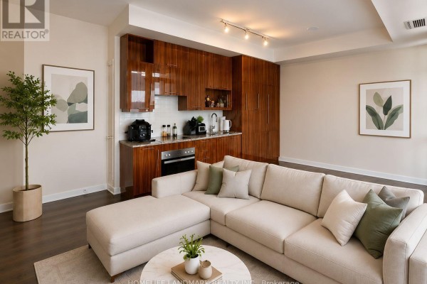 Living area with sectional sofa facing a modern kitchen with wood cabinetry and stainless steel appliances. - 418 - 199 Richmond Street W, Toronto