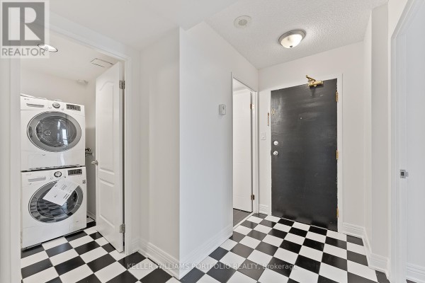 Apartment hallway featuring black and white checkered floor tiles and a stacked washer and dryer unit. - 418 - 2550 Lawrence Avenue E, Toronto