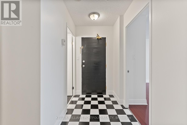 Hallway of an apartment with black and white checkered flooring and a dark wood door. - 418 - 2550 Lawrence Avenue E, Toronto