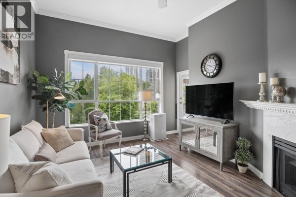 Living room with grey walls, a fireplace, sofa, armchair, and large window overlooking trees. - 418 2995 Princess Crescent, Coquitlam