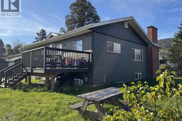 Rear exterior of the house with a large wooden deck and stairs, view of backyard. - 4186 2nd Avenue, Smithers
