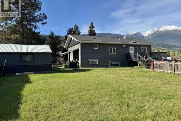 View of the house from the backyard, showing a shed, detached garage, and mountain backdrop. - 4186 2nd Avenue, Smithers