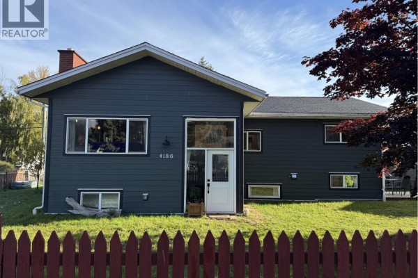 Front view of the house with dark grey siding, white front door, and large windows. - 4186 2nd Avenue, Smithers