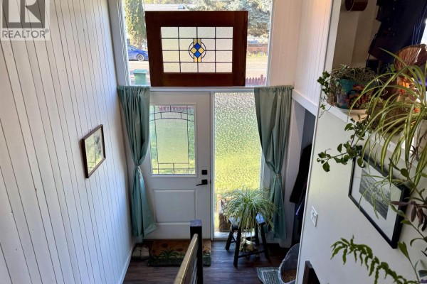 Interior entryway with white paneled walls, glass front door, and a stained-glass window above. - 4186 2nd Avenue, Smithers