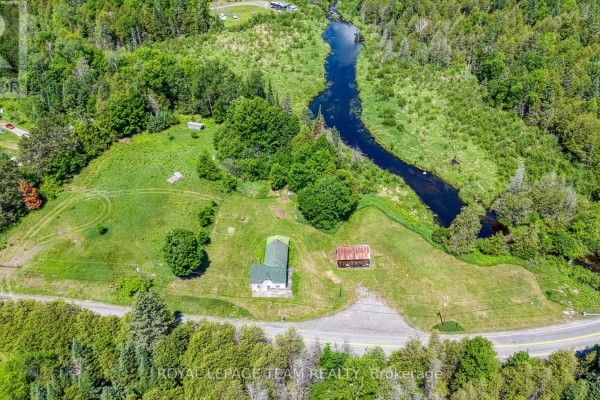 Aerial view of the property with a creek, green fields, and a white house. - 4186 Tatlock Road, Lanark Highlands