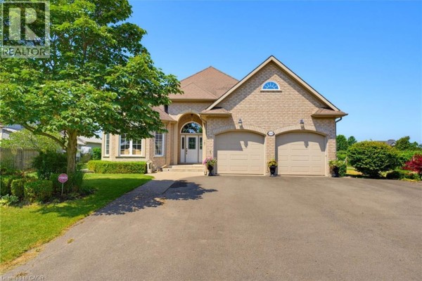 Brick bungalow exterior with a paved driveway, manicured lawn, and green trees. - 4188 Victoria Avenue, Vineland Station