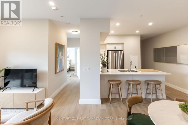 View of the living area, hallway, and kitchen with light wood flooring and neutral wall colors. - 419 - 230 North Centre Road, London North