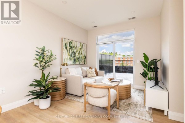 Living room with beige sofa, patterned rug, and large sliding glass doors opening to a balcony. - 419 - 230 North Centre Road, London North