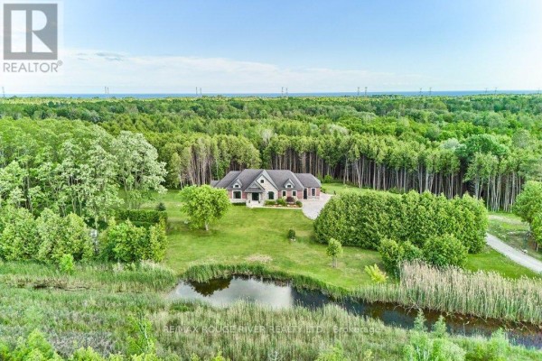 Aerial view of a brick house nestled in a wooded area with a pond. - 4199 Highway #2, Clarington