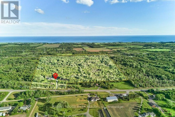 Aerial overview of a large property with a brick house, wooded areas, and distant water. - 4199 Highway #2, Clarington