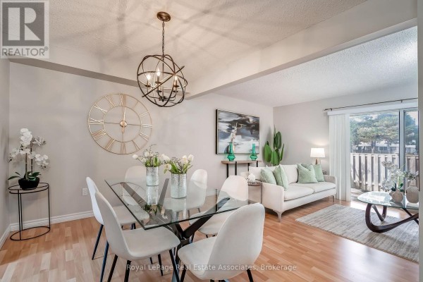Living and dining area with glass table, white chairs, couch, and patio door. - 42 - 2779 Gananoque Drive, Mississauga