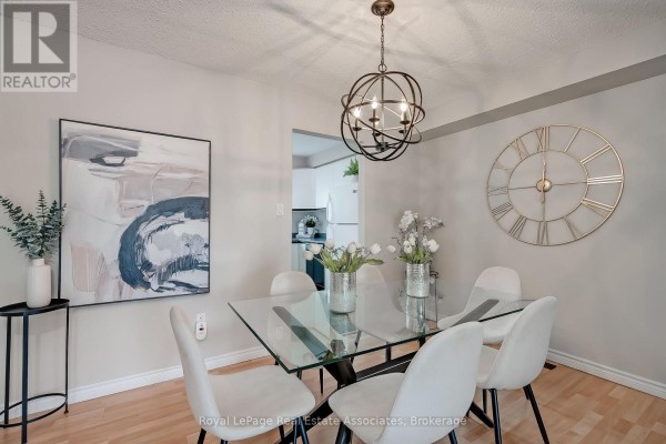 Dining area with glass table, white chairs, artwork, and open doorway to kitchen. - 42 - 2779 Gananoque Drive, Mississauga