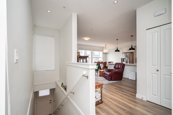 View from staircase landing looking into an open-concept living and kitchen area with large windows. - 42 8372 202b Street, Langley