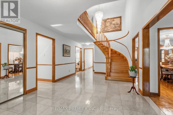 Spacious foyer with a curved wooden staircase, chandelier, tiled floor, and wooden trim. - 42 Burgosa Court, Vaughan