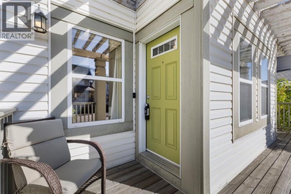 Close-up of a light green front door with a glass insert and a covered porch with a chair. - 42 Copperpond Place Se, Calgary
