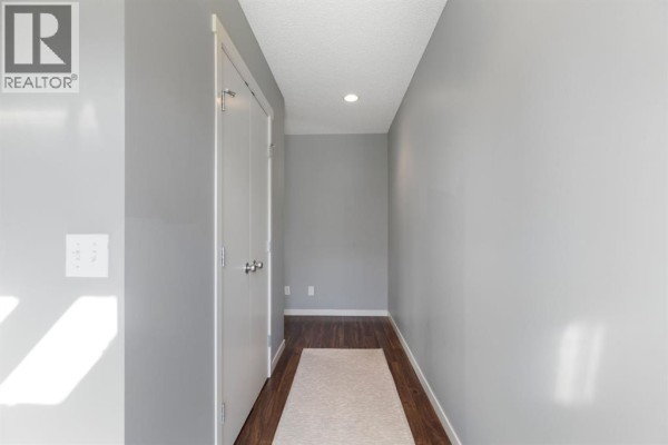 Narrow hallway with grey walls, dark wood floors, and white double doors on the right. - 42 Copperpond Place Se, Calgary
