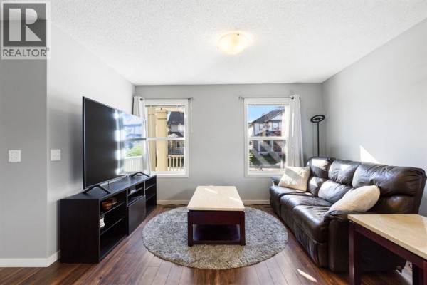 Living room with grey walls, dark leather sofa, coffee table, large television, and dark wood floors. - 42 Copperpond Place Se, Calgary