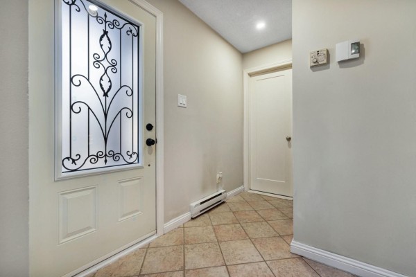 Interior view of a beige entryway with a white door, tiled floor, and thermostat. - 42 Rue De Loranger, Gatineau