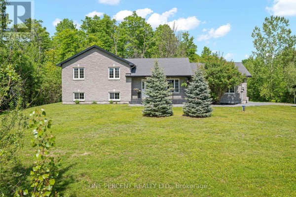 Front exterior view of a grey brick house with a sloped lawn and mature trees. - 42 Stonewalk Drive, North Grenville