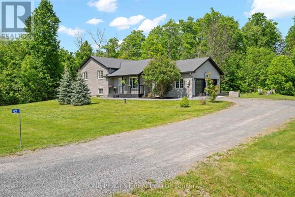 View of the house and gravel driveway from the side, with mature trees and greenery. - 42 Stonewalk Drive, North Grenville