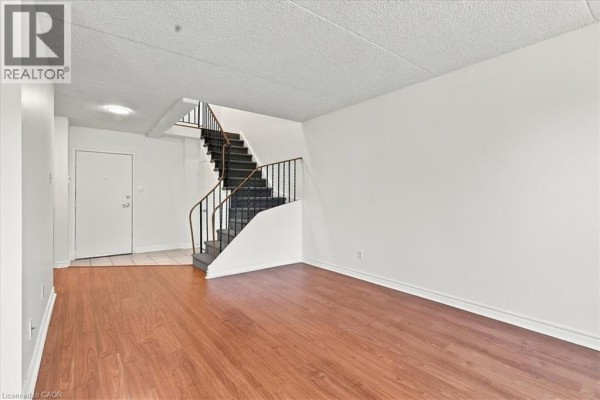 Apartment living area with wood flooring, front door, and carpeted staircase. - 42 Tannery Street E Unit# 246, Cambridge