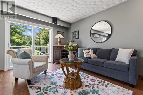 Living room with a blue sofa, armchair, coffee table, and a sliding glass door leading outside. - 42 Webster Street, Kincardine