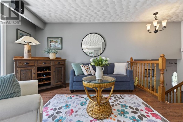 Living room with a blue sofa, armchair, wooden sideboard, and view of the staircase. - 42 Webster Street, Kincardine