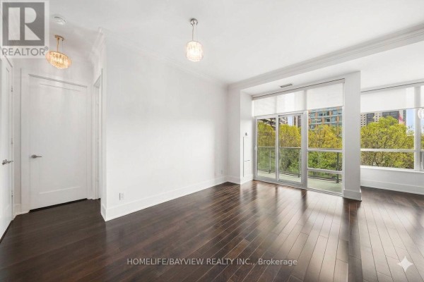 Empty living space with dark hardwood floors, white walls, and large windows overlooking trees. - 420 - 120 Homewood Avenue, Toronto