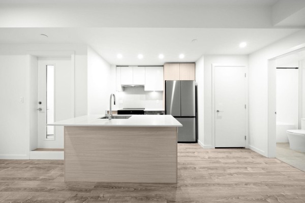 Apartment interior with kitchen, island, and view into a bathroom with a toilet. - 420 10828 139a Street, Surrey