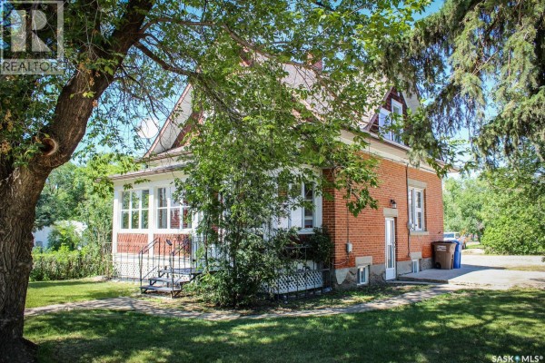 Side exterior view of the residential house with green lawn and trees. - 420 Burrows Avenue W, Melfort