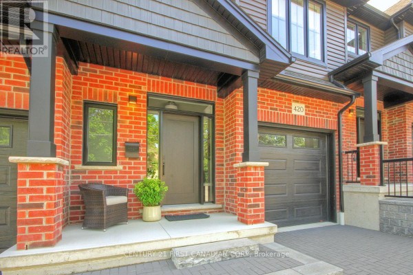 Close-up of a townhouse entrance with red brick, dark grey siding, and a black garage door. - 420 Old Wonderland Road, London South