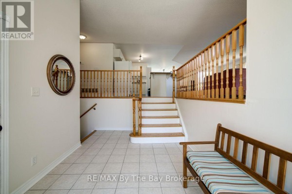 Foyer with white tiled floor, wooden bench with teal cushion, and double entry doors. - 420 Ramblewood Drive, Wasaga Beach