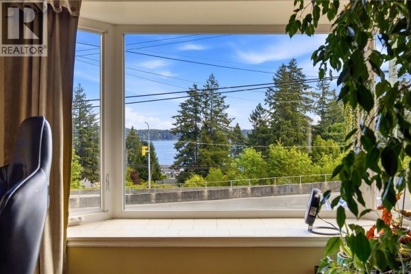 View of a body of water and trees through a large bay window with brown curtains. - 420 Strang Dr, Ladysmith