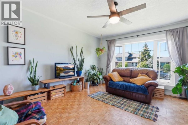 Living room with parquet floors, multiple plants, and a large wooden armoire. - 420 Summerwood Place Se, Airdrie