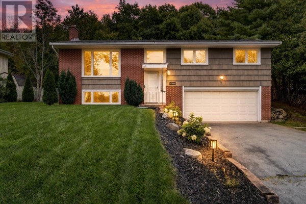 Front view of the split-level home at dusk, with interior lights illuminating the windows and landscaping. - 4200 Highway 2, Wellington