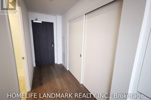 Apartment hallway with dark wood floors, a dark front door, and white sliding closet doors. - 4201 - 20 Lombard Street, Toronto