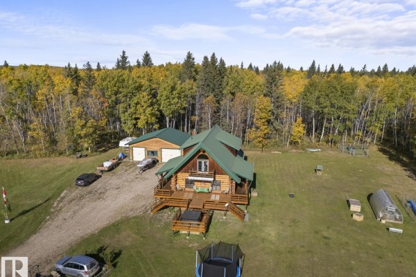 Aerial view of the log cabin, garage, and surrounding property with a wooded landscape. - 42030 Twp Rd 604, Rural Bonnyville M D 