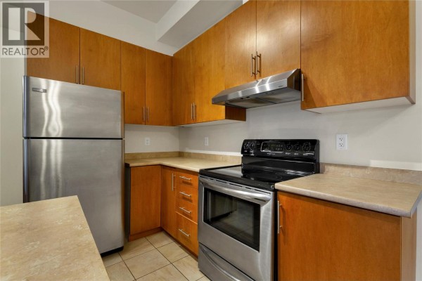 Kitchen with stainless steel refrigerator, black range, and light wood cabinetry. - 4205 27 Street Unit# 103, Vernon
