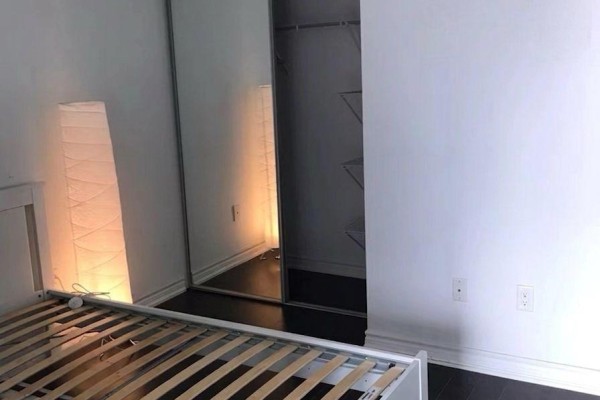 Bedroom corner showing a bed frame, floor lamp, and a mirrored closet. - 4206 - 386 Yonge Street, Toronto