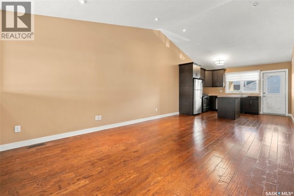 Hallway view looking towards kitchen with hardwood floors, beige walls, and open doorway. - 4207 Green Apple Drive E, Regina