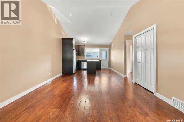Living room and kitchen area with hardwood floors, dark wood cabinets, and stainless steel appliances. - 4207 Green Apple Drive E, Regina