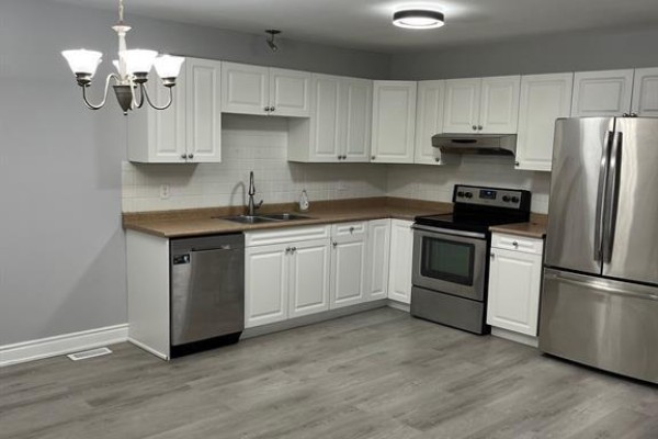 L-shaped kitchen with white cabinets, stainless steel appliances, and grey floor. - 4207 Whiskey Avenue, Windsor