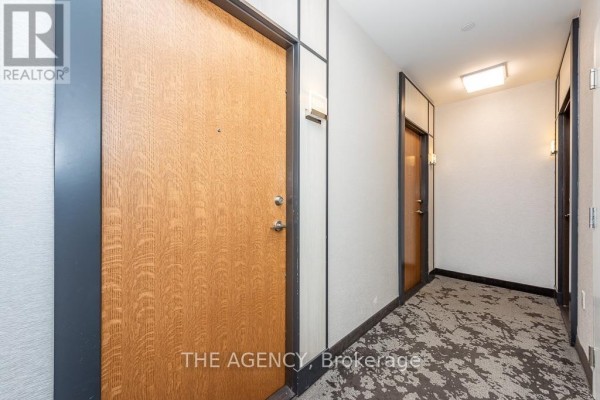 Apartment hallway with wood-grain door, textured walls, and patterned carpet. - 4208 - 20 Shore Breeze Drive, Toronto