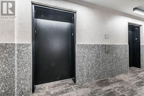 Interior hallway with two dark elevator doors and speckled grey wall panels. - 421 - 3008 William Cutmore Boulevard, Oakville